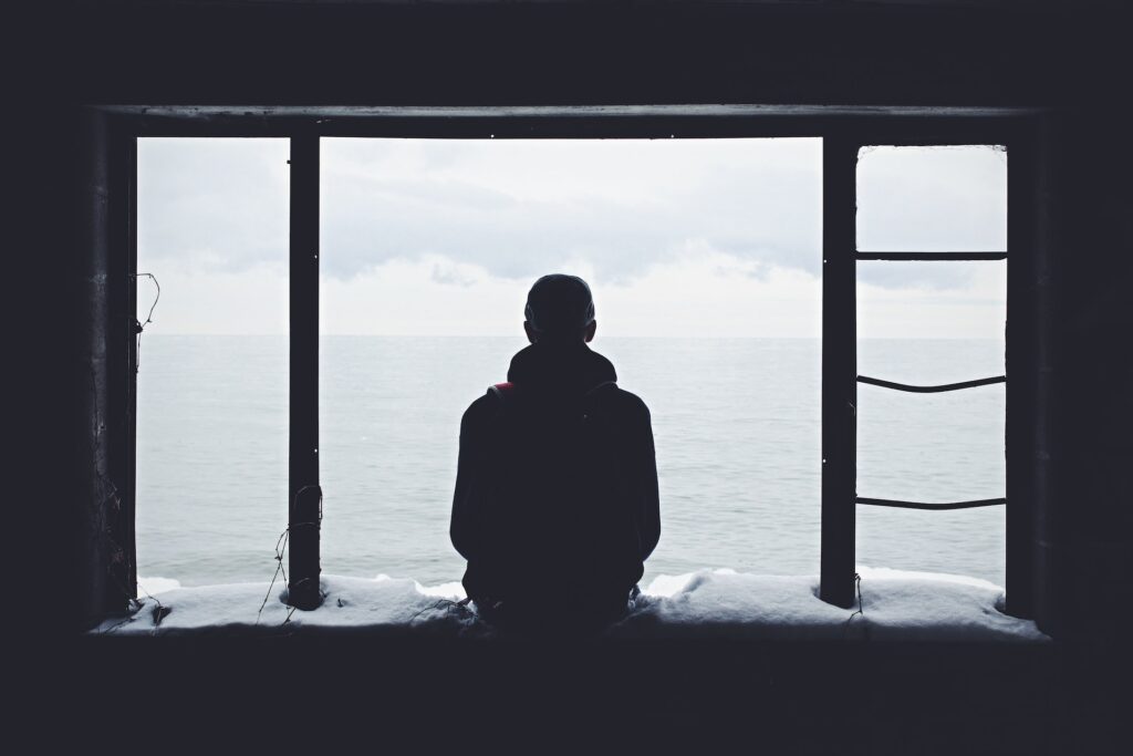 man sitting on window ledge looking at snowy sea - Photo by Noah Silliman on Unsplash