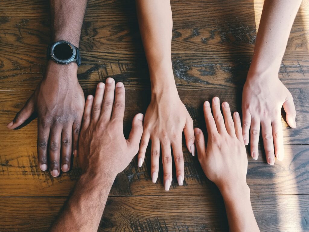 Five human hands on a wooden table representing the Found Family trope - Photo by Clay Banks on Unsplash