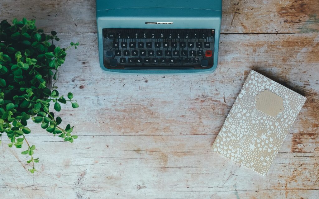 Plant, typewriter, and notebook on a wooden table - the best writing advice - photgraph by Annie Spratt for Unsplash