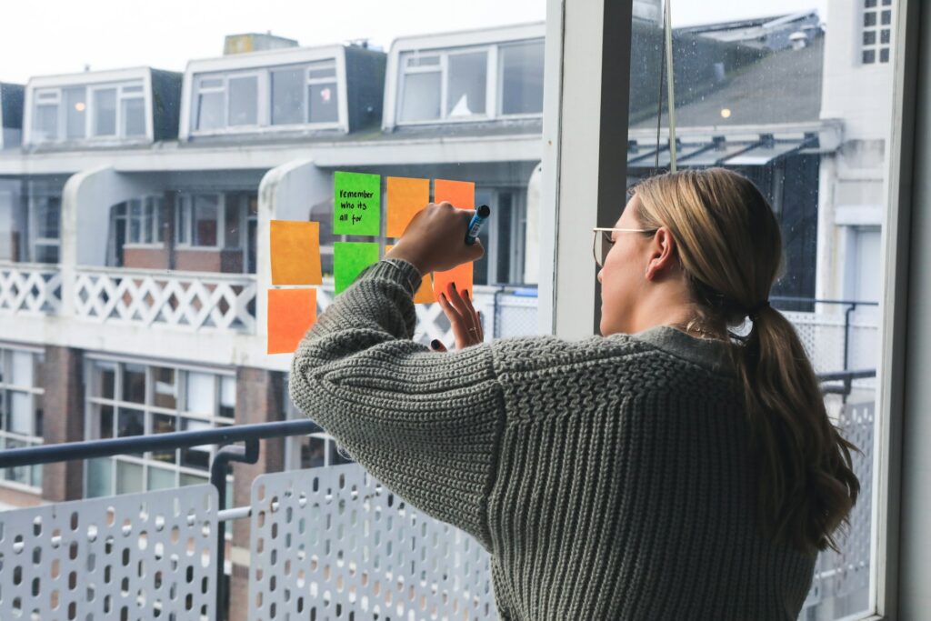 Woman brainstorming from a writing prompt on post-it notes on a window - Photo by Magnet.me on Unsplash

